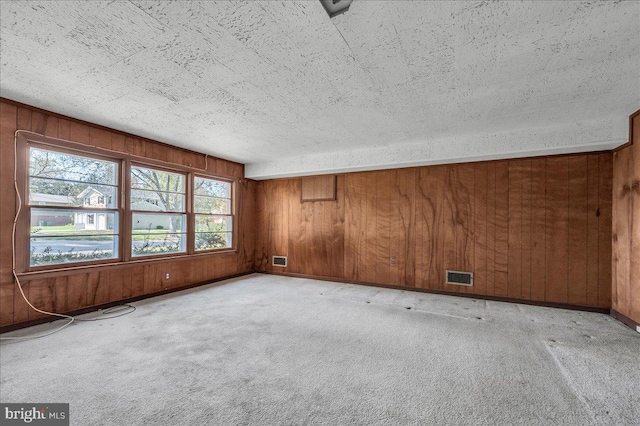 carpeted spare room with wooden walls, visible vents, and a textured ceiling