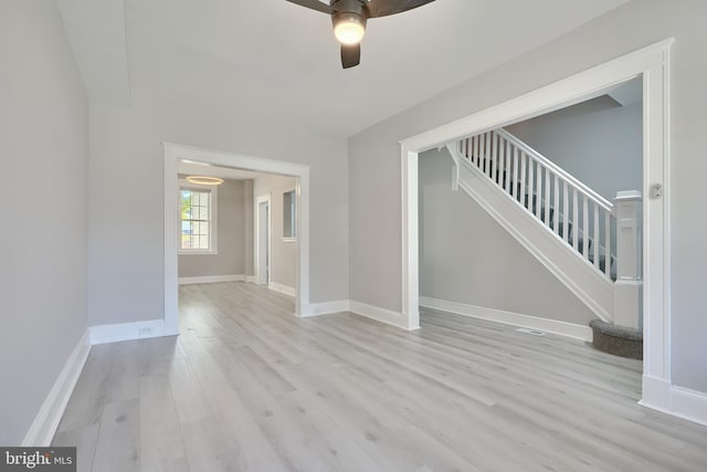 unfurnished living room featuring baseboards, light wood finished floors, ceiling fan, and stairs