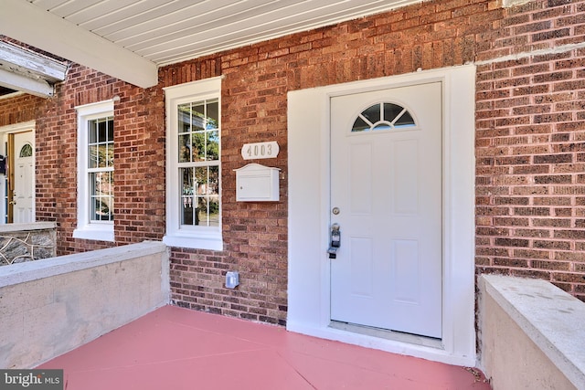view of exterior entry featuring brick siding and covered porch