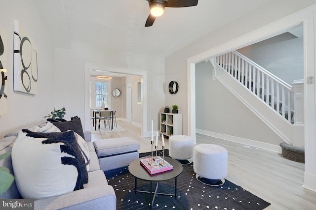 living area featuring a ceiling fan, stairs, and wood finished floors