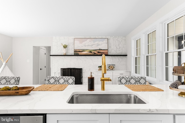 kitchen with light stone countertops, white cabinetry, a large fireplace, a sink, and dishwasher