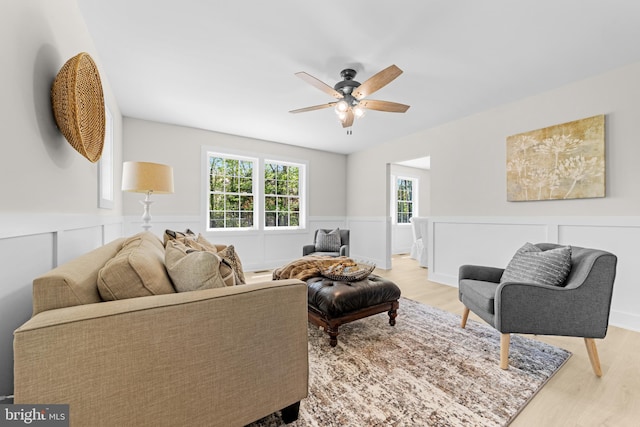 living area with a wainscoted wall, a ceiling fan, and wood finished floors