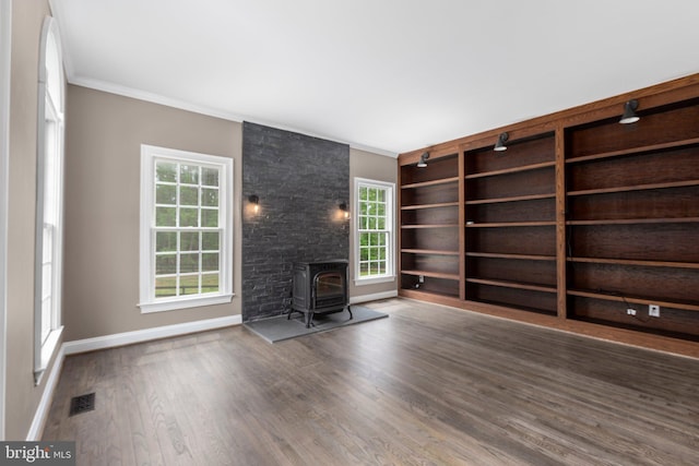 unfurnished living room featuring a wood stove, ornamental molding, wood finished floors, healthy amount of natural light, and baseboards