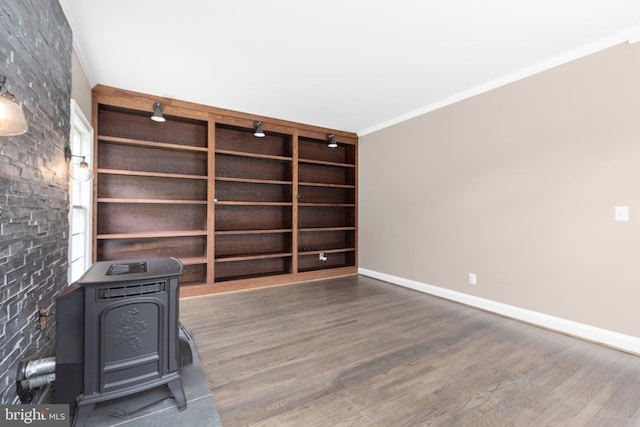 spare room featuring a wood stove, ornamental molding, wood finished floors, and baseboards