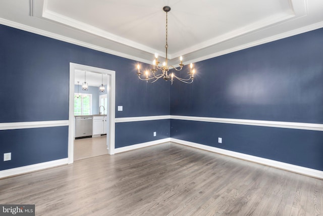 spare room featuring a tray ceiling, a chandelier, wood finished floors, and crown molding