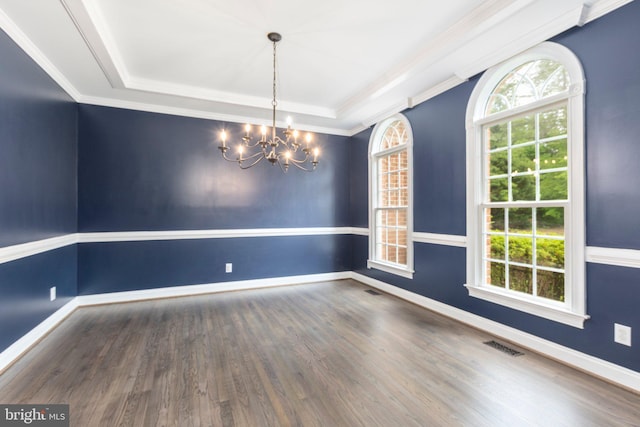 empty room featuring a raised ceiling, a chandelier, wood finished floors, baseboards, and ornamental molding