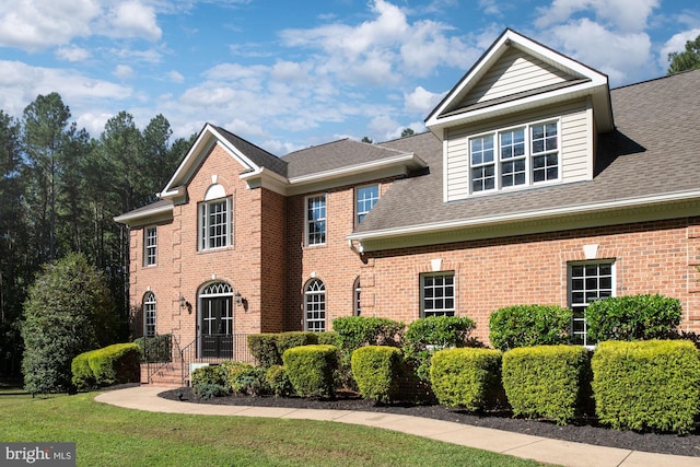 colonial home with brick siding, a shingled roof, and a front lawn