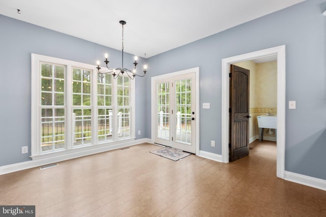 unfurnished dining area featuring a chandelier, baseboards, and french doors