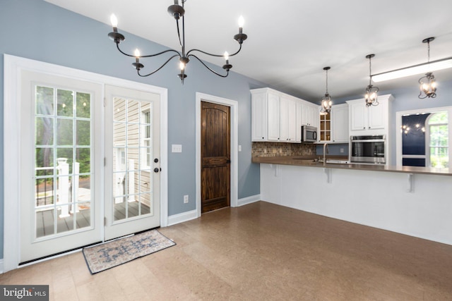 kitchen with stainless steel appliances, a chandelier, decorative backsplash, dark countertops, and white cabinetry