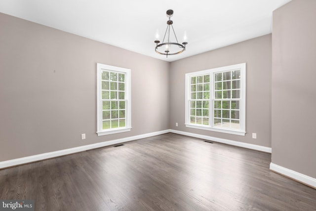 empty room with a chandelier, healthy amount of natural light, baseboards, and dark wood finished floors