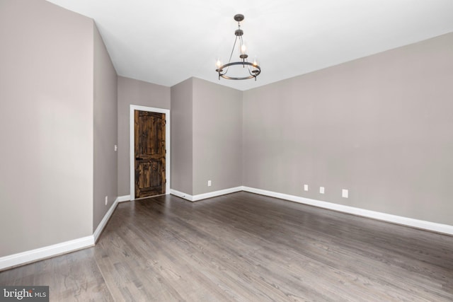 spare room featuring a chandelier, baseboards, and wood finished floors
