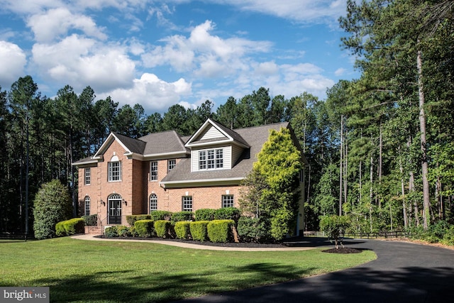 colonial house with brick siding, a front lawn, and a shingled roof