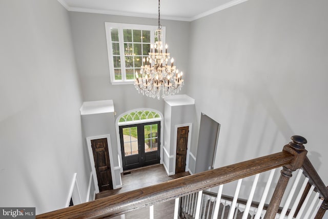 foyer entrance featuring a chandelier, a towering ceiling, french doors, wood finished floors, and ornamental molding
