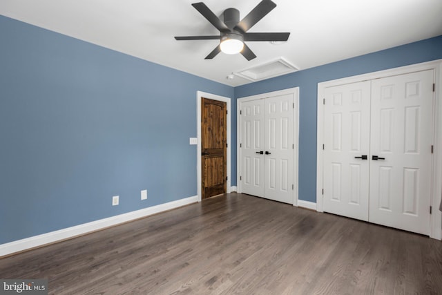unfurnished bedroom with two closets, wood finished floors, baseboards, attic access, and a ceiling fan