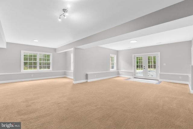 unfurnished living room featuring light colored carpet, french doors, baseboards, and plenty of natural light