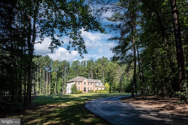 view of front of property with a wooded view, a front lawn, and asphalt driveway