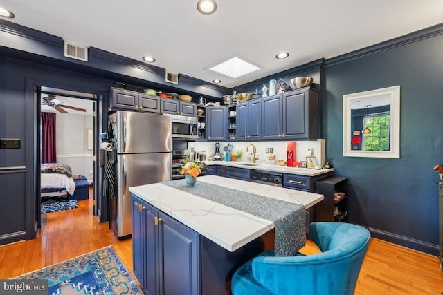 kitchen with a kitchen island, visible vents, a sink, light wood finished floors, and stainless steel appliances