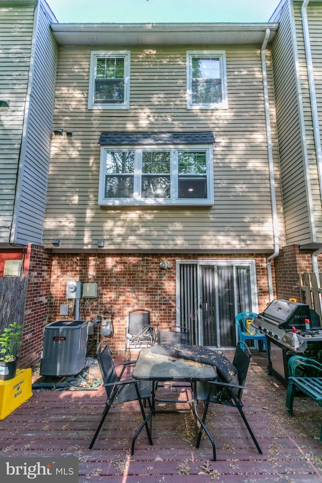 rear view of house with cooling unit, a deck, and brick siding