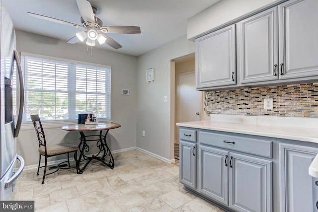 kitchen with stainless steel fridge, a ceiling fan, baseboards, decorative backsplash, and gray cabinetry