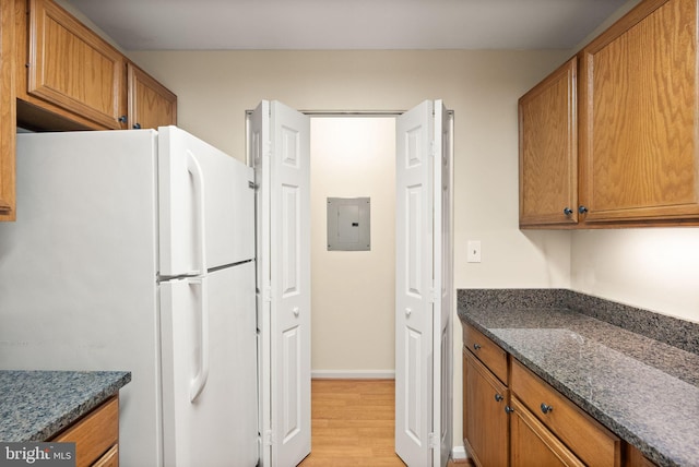 8075 Lacy Dr Unit 303, Manassas, VA 20109 - kitchen with freestanding refrigerator, light wood-style flooring, dark stone countertops, electric panel, and brown cabinets