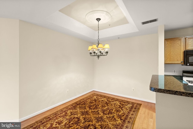 8075 Lacy Dr Unit 303, Manassas, VA 20109 - unfurnished dining area featuring a tray ceiling, light wood-style flooring, baseboards, visible vents, and a chandelier