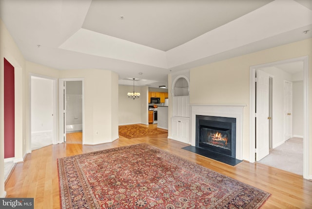 8075 Lacy Dr Unit 303, Manassas, VA 20109 - unfurnished living room featuring baseboards, light wood finished floors, a raised ceiling, a notable chandelier, and a fireplace with flush hearth