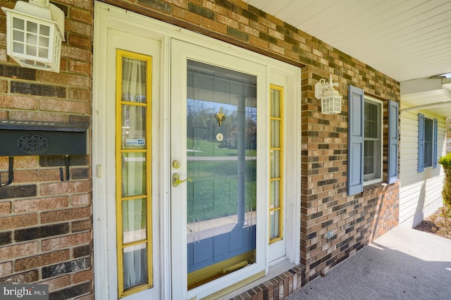 doorway to property featuring brick siding and a porch