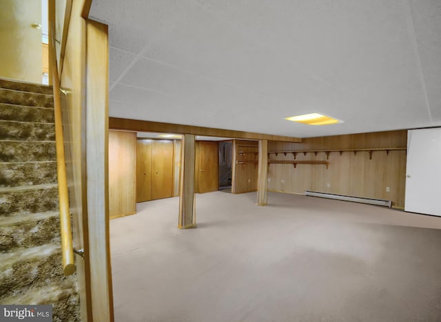 finished below grade area featuring stairs, wooden walls, and a baseboard heating unit