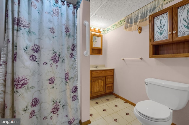full bath featuring tile patterned flooring, vanity, toilet, baseboards, and a drop ceiling