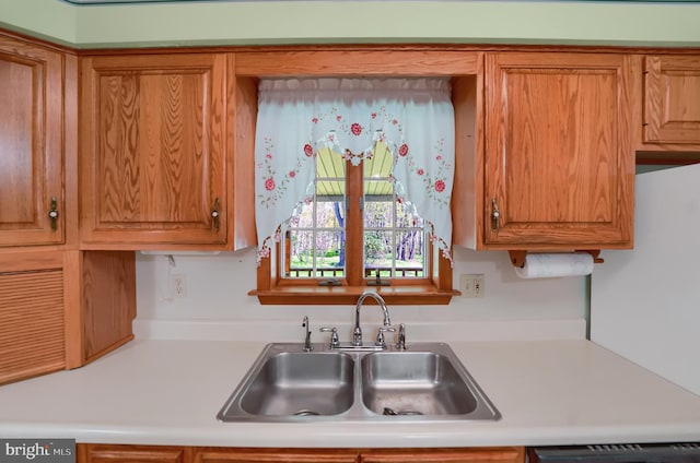 kitchen featuring a sink, light countertops, brown cabinets, and dishwashing machine