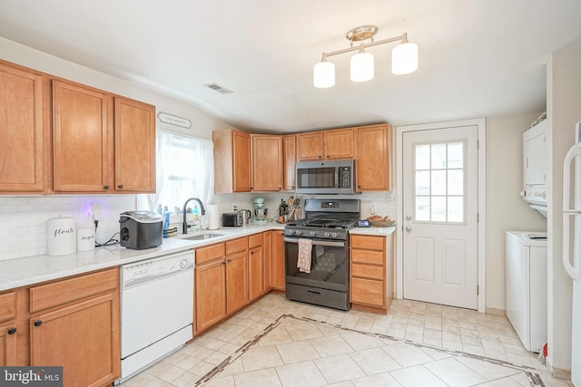 kitchen featuring visible vents, stacked washer and dryer, light countertops, a sink, and stainless steel appliances