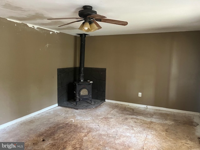 unfurnished living room featuring ceiling fan, baseboards, and a wood stove