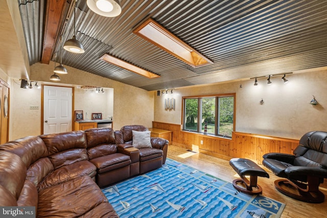 living area featuring rail lighting, lofted ceiling with skylight, wood walls, hardwood / wood-style floors, and wainscoting