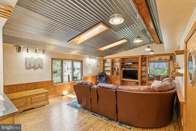 living room featuring track lighting, wood finished floors, vaulted ceiling with skylight, wainscoting, and wood walls