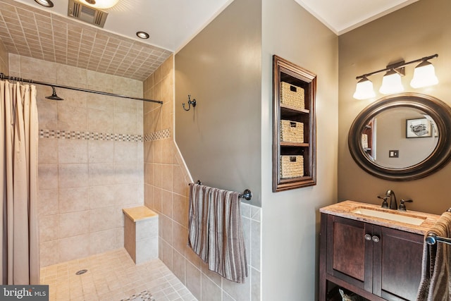 bathroom featuring visible vents, tiled shower, and vanity