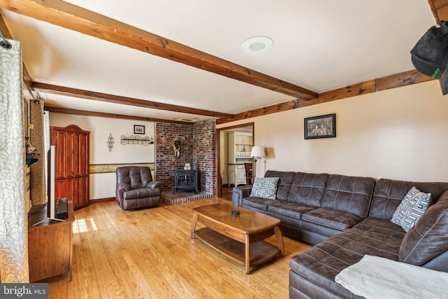 living room with beam ceiling, a wood stove, light wood finished floors, and baseboards