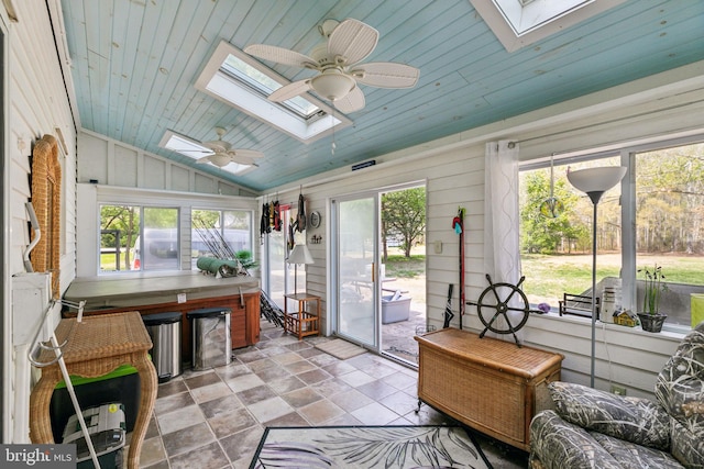 sunroom / solarium with lofted ceiling with skylight, a ceiling fan, wooden ceiling, and stone finish floor