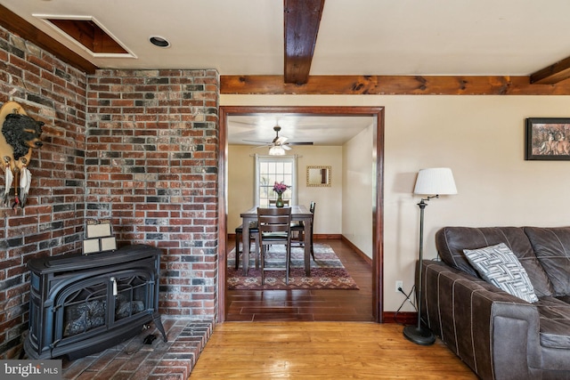 living room with a wood stove, light wood finished floors, beam ceiling, and baseboards