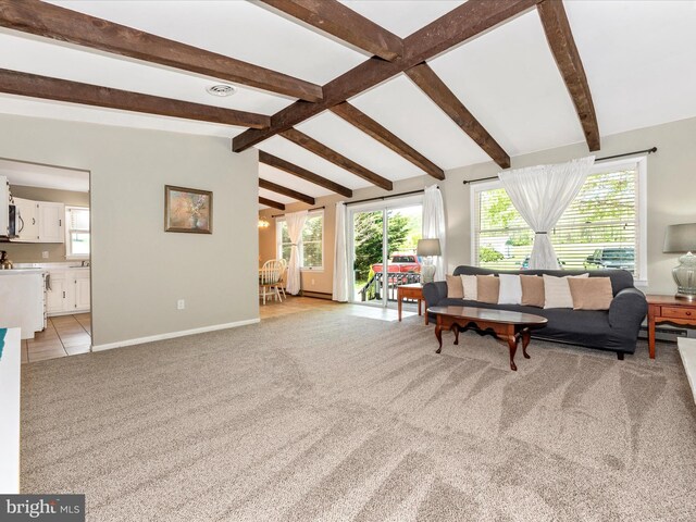 living area featuring baseboards, lofted ceiling with beams, a healthy amount of sunlight, and light carpet