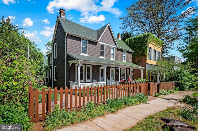 view of front of property with a porch, a fenced front yard, a shingled roof, and a chimney