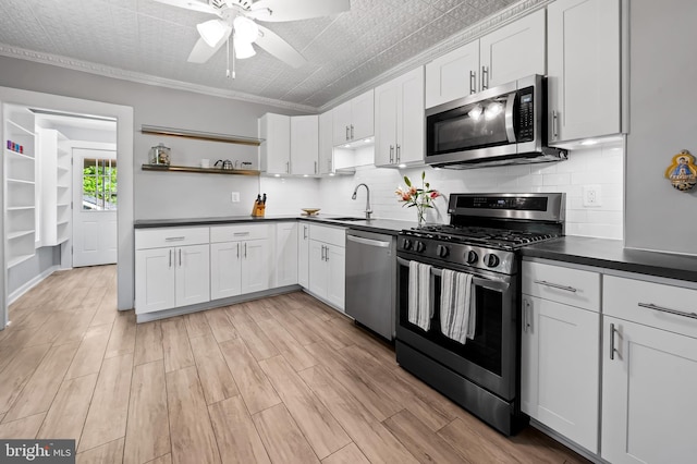 kitchen with a ceiling fan, a sink, open shelves, dark countertops, and appliances with stainless steel finishes
