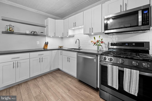 kitchen with open shelves, appliances with stainless steel finishes, dark countertops, a sink, and an ornate ceiling