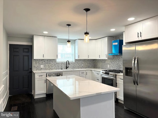 kitchen with a sink, appliances with stainless steel finishes, wall chimney range hood, and white cabinetry