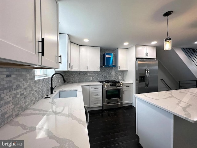 kitchen featuring wall chimney range hood, light stone countertops, hanging light fixtures, a sink, and stainless steel appliances