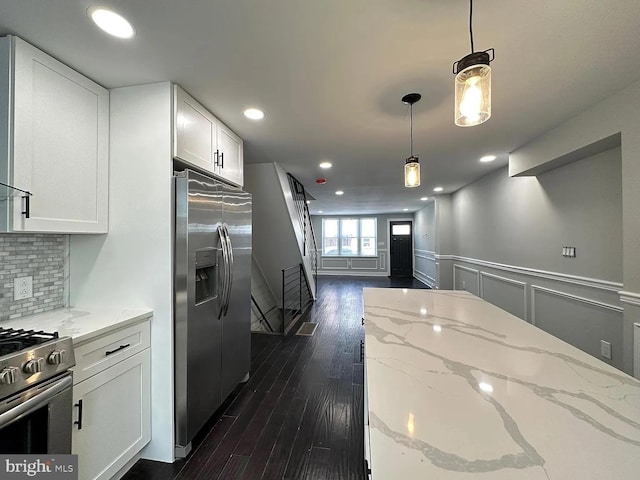 kitchen featuring pendant lighting, wainscoting, light stone countertops, white cabinetry, and appliances with stainless steel finishes