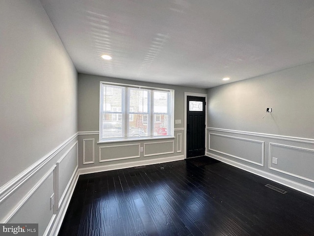spare room with a decorative wall, visible vents, a wainscoted wall, and dark wood-type flooring