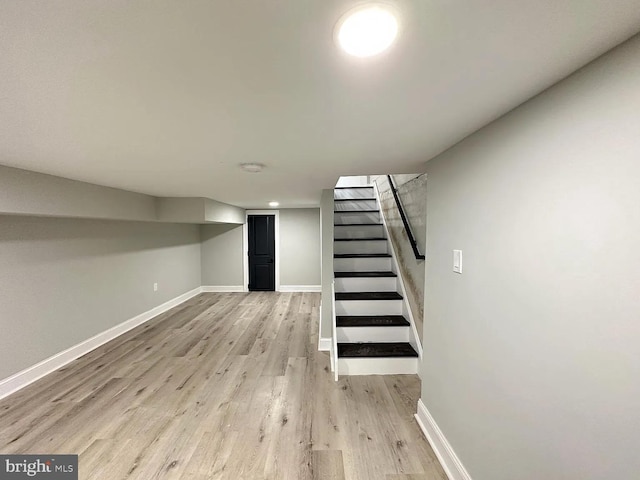 finished below grade area featuring baseboards, light wood-type flooring, and stairs