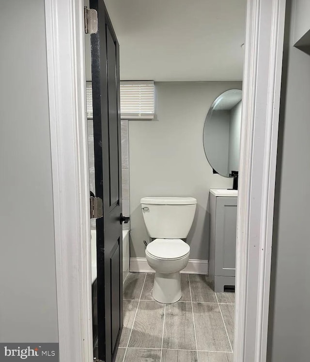 half bathroom featuring vanity, wood tiled floor, baseboards, and toilet