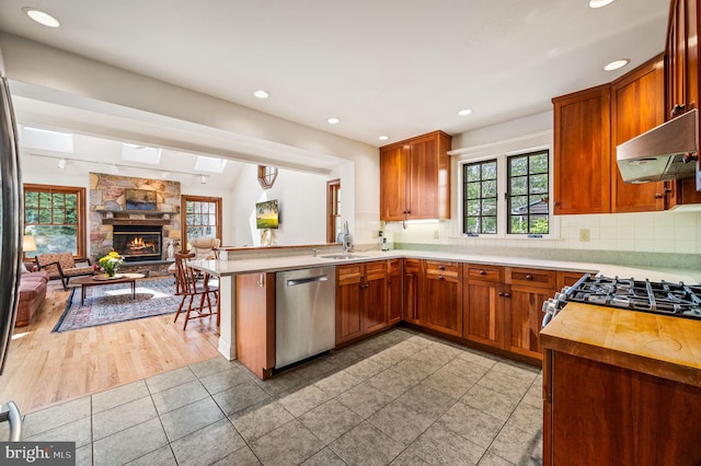 kitchen with a sink, stainless steel appliances, under cabinet range hood, a peninsula, and open floor plan
