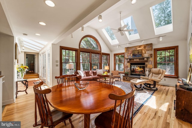 dining room featuring a fireplace, baseboards, light wood finished floors, and vaulted ceiling with skylight